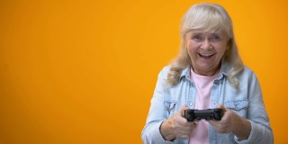 积极乐观的老年妇女玩电脑游戏，拿着操纵杆，小玩意