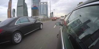 这辆车沿着高速公路行驶，旁边是一辆豪华车沿着摩天大楼行驶。从车身的侧视图