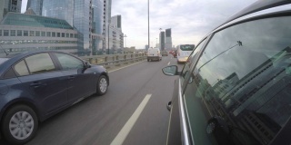 汽车在高峰时间的高速公路上行驶，旁边是摩天大楼。从车身的侧视图
