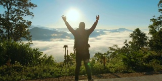 空中男性摄影师站在山上，举起他的手在早晨的日出