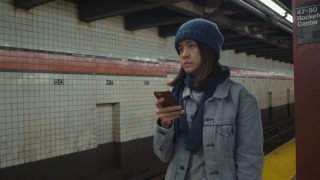 年轻的亚洲女子在地铁站台上用手机等待和发短信。视频素材模板下载