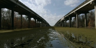 在阳光明媚但部分多云的天空下，在南路易斯安那州阿查法拉亚河流域沼泽被柏树林包围的阿查法拉亚河流域沼泽上，用卡车向前行驶的无人机拍摄的从东到西的布罗桥(10号州际公路)