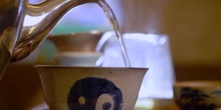 在中国茶道上，男子的手从茶壶里倒热水到盖碗里，这是由宜兴陶土手工绘制的阴阳标志