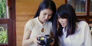 快乐的亚洲女性朋友在咖啡厅咖啡厅看数码相机照片