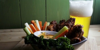 一碗健康的烤鸡翅配辣汁芹菜和胡萝卜条，再来一杯啤酒