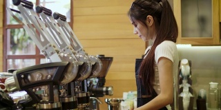 年轻微笑的亚洲女性咖啡师或女性咖啡所有者使用咖啡机，并在咖啡店咖啡厅看着镜头