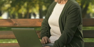 上了年纪的女性敲打笔记本电脑键盘，坐在长椅上，上网搜索，应用程序