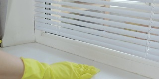 一个戴着黄色橡胶手套的女人用抹布擦拭窗台