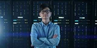 在现代数据中心:IT工程师站在他身后的服务器机架，交叉手臂。专业的IT专家，在现代数据中心工作，拥有创新的技术。