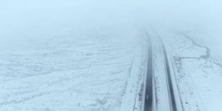 无人机拍摄的是一辆汽车在空旷的雪地里行驶在高速公路上的画面