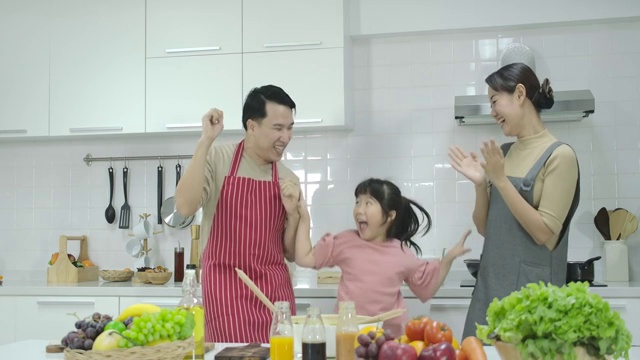 快乐快乐的亚洲家庭一起跳舞，在厨房做饭。