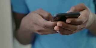 近距离拍摄的非洲裔美国青少年穿着蓝色t恤在智能手机上发短信。