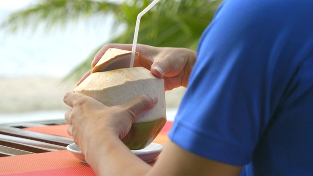 坐在沙滩上喝椰子汁的男人。