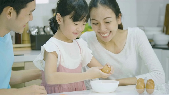 微笑的亚洲父亲，母亲和女儿喜欢在厨房一起准备健康的晚餐。母亲教女儿做饭。