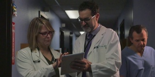 在繁忙的诊所或医院里，两名医生在平板电脑上讨论一个病例