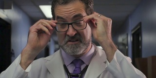英俊的男医生摘掉眼镜站在医院走廊
