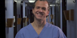 一个穿着蓝色手术服的男人在诊所里微笑着看着摄像机