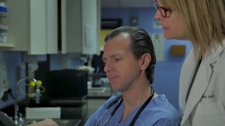 女医生一边看平板电脑一边与男护士或医生交谈视频素材模板下载