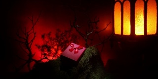 情人节的爱情概念。美丽的艺术品装饰小礼品盒和古老的灯笼在晚上。礼盒在晚上用石头装饰假森林。空空间选择焦点
