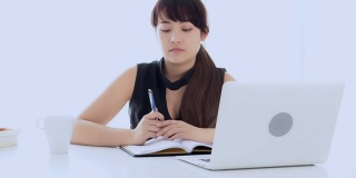 美丽的亚洲女人微笑着坐在客厅学习和学习写笔记本在家里，女孩家庭作业，商业女人思考的想法与笔记本电脑在桌子上工作，教育理念。