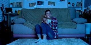 惊恐的青少年在深夜看恐怖电影，吃爆米花，情绪低落