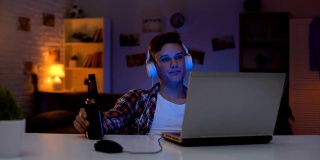十几岁的男孩在电脑上看电影，喝啤酒，吃零食，浪费时间