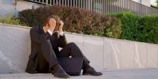 慢镜头:一个悲伤的男人坐在人行道上，双手抱头。
