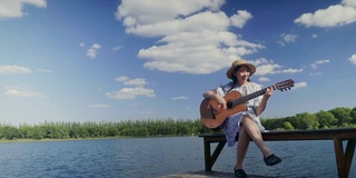 快乐的年轻亚洲女人在湖边和蓝天的背景，复制空间演奏古典吉他