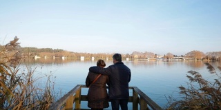 一对老年夫妇凝视着码头旁边的湖水