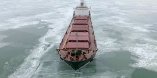 在极端冬季条件下在冰冻海面上航行的货船航拍。在破冰船造成的狭窄航道中航行。北方寒冷冬季的水运