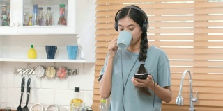 年轻美丽的亚洲女性戴着耳机，使用智能手机，在厨房喝咖啡，人和科技，Z一代的生活方式