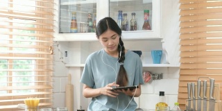 年轻美丽的亚洲女性站在厨房里使用数字平板电脑和耳机，人们和科技，Z一代的生活方式