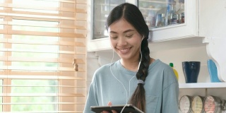 年轻美丽的亚洲女人站在厨房里使用平板电脑和耳机，人们和科技，Z一代的生活方式