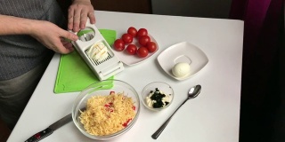 一个男人用切蛋器切煮熟的鸡蛋。用蟹肉棒，奶酪，鸡蛋和西红柿做沙拉。