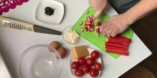 一个男人正在切蟹肉条。用蟹肉棒，奶酪，鸡蛋和西红柿做沙拉。
