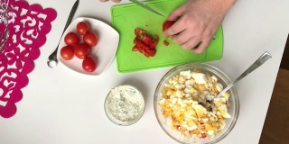 一个男人在砧板上切西红柿。用蟹肉棒，奶酪，鸡蛋和西红柿做沙拉。