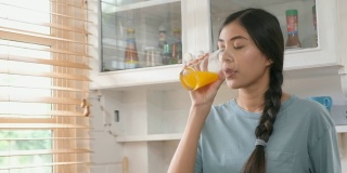 年轻美丽的亚洲女人在厨房喝橙汁的特写，健康的生活方式