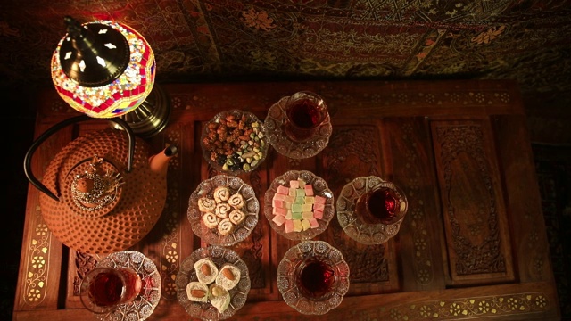 阿拉伯茶在玻璃和东方小吃在复古的木制表面。东方茶的概念。低灯光休息室内部地毯。空的空间。视图从上