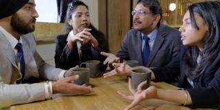商务印度同事坐在咖啡馆里喝着他们的热饮料在他们的杯子里，他们讨论友好和有趣的事情