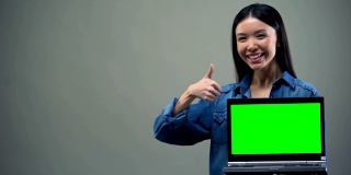 微笑的女人举起大拇指，拿着绿屏笔记本电脑，在线教育
