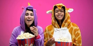 两个穿着独角兽和长颈鹿睡衣的女人一边吃着爆米花一边看喜剧