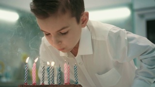 男孩在生日蛋糕上吹蜡烛。生日快乐男孩吹蜡烛火焰视频素材模板下载