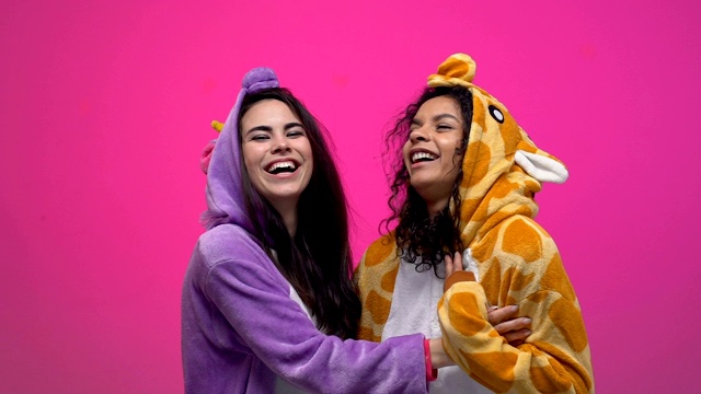 两个穿着独角兽和长颈鹿睡衣的女人笑着拥抱着，友谊