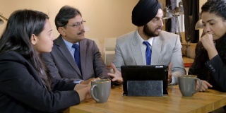 一位脸色铁青、包着黑色头巾的锡克教徒队长在展示一台触摸屏平板电脑上的数字时，正在嘲笑和斥责他的团队成员，因为他们似乎很愚蠢，无法给他留下深刻印象