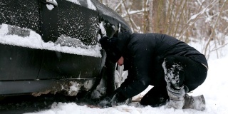 一名男子在汽车车轮附近清理积雪。