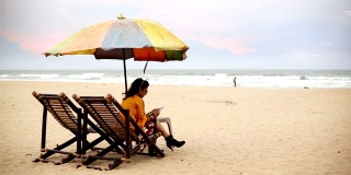 一名年轻女子坐在卡兰古特海滩的躺椅上，正在使用智能手机