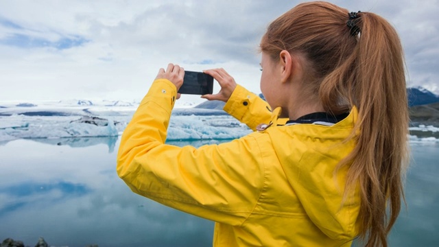 一名女子用智能手机拍摄冰川湖中漂浮的冰山