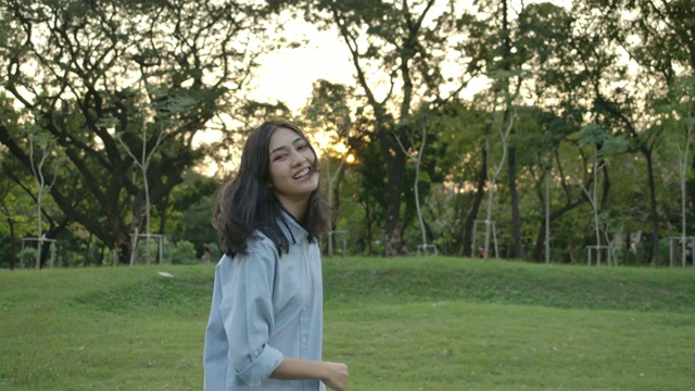 慢动作拍摄的年轻迷人的亚洲女人在一个夏天的公园在日落。美丽的女孩在户外享受大自然。