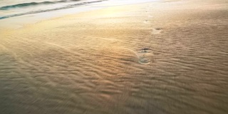 夕阳的海浪把脚印冲刷在金色的沙滩上
