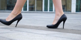 年轻女商人的脚穿着高跟鞋走在城市的街道上。苗条女性的腿在黑色高跟鞋上走在城市。女孩走着去上班。低角度视角慢动作特写